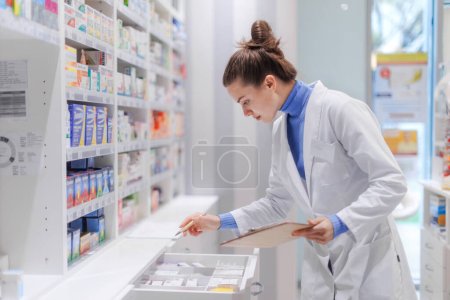 Young pharmacist checking medicine stock in a pharmacy.