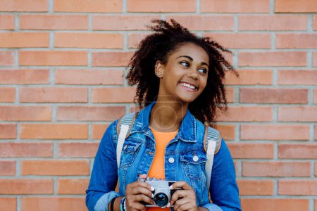 Foto de Multiracial girl standing in front of brick wall with a camera, and posing. - Imagen libre de derechos