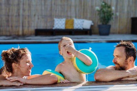 Photo for Happy young family spending summer time together in a pool. - Royalty Free Image
