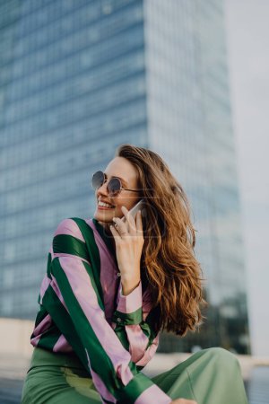 Téléchargez les photos : Portrait de belle jeune femme avec smartphone en plein air dans une ville, au coucher du soleil. - en image libre de droit