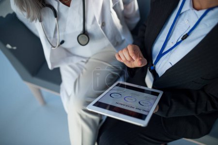 Foto de Vista de ángulo alto de la mujer de negocios que muestra el gráfico en tableta digital al médico en el hospital. - Imagen libre de derechos
