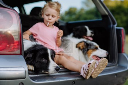 Téléchargez les photos : Petite fille et ses chiens assis dans une voiture, préparés pour un voyage en famille, - en image libre de droit