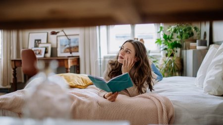 Foto de Mujer joven disfrutando del tiempo libre en su apartamento, leyendo un libro. - Imagen libre de derechos