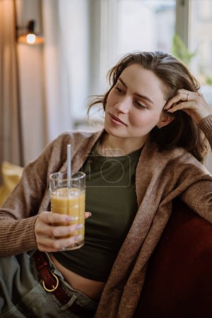 Foto de Mujer joven sentada en el sofá con una bebida. - Imagen libre de derechos