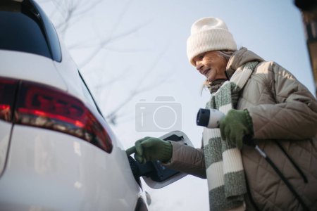 Téléchargez les photos : Gros plan d'une femme âgée rechargeant une voiture électrique. - en image libre de droit