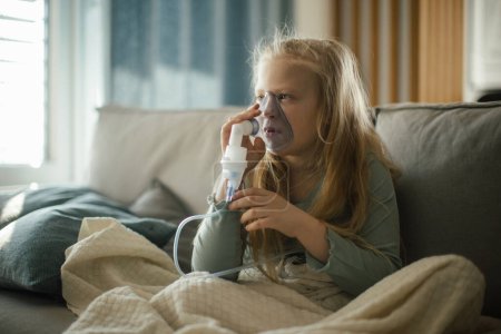 Téléchargez les photos : LIttle fille malade en utilisant un inhalateur pendant la grippe. - en image libre de droit