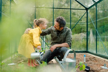 Foto de A father learning his little daughter to care about organic plants in eco greenhouse, sustainable lifestyle. - Imagen libre de derechos