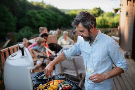 Photo for Mature man grilling food at family bbq party. - Royalty Free Image
