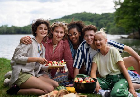 Foto de A group of multiracial young friends camping near lake and and having barbecue together. - Imagen libre de derechos