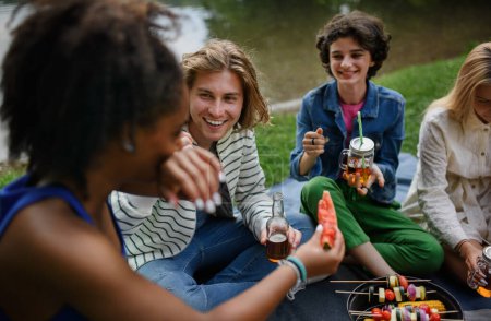Téléchargez les photos : A group of multiracial young friends camping near lake and and having barbecue together. - en image libre de droit