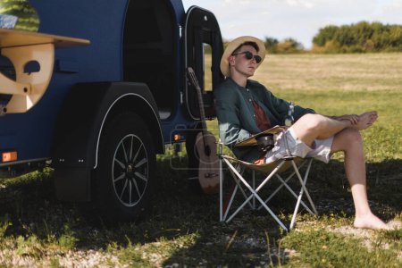 Photo for Young man sitting in front of a van enjoying summer time. - Royalty Free Image