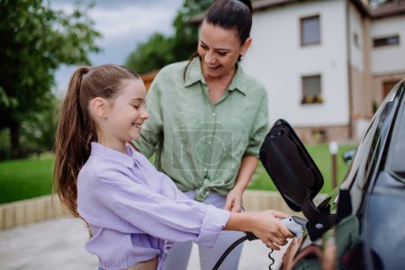 Photo for Happy mother showing her daughter how to charge their electric car. - Royalty Free Image
