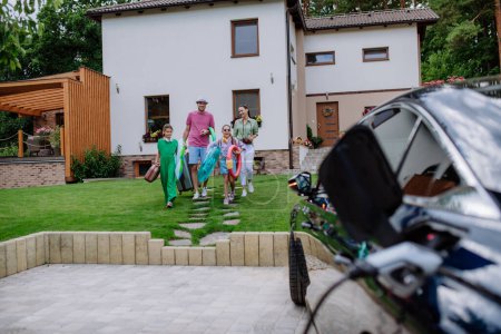 Téléchargez les photos : Famille heureuse se préparant pour des vacances tandis que leur voiture électrique charge. - en image libre de droit