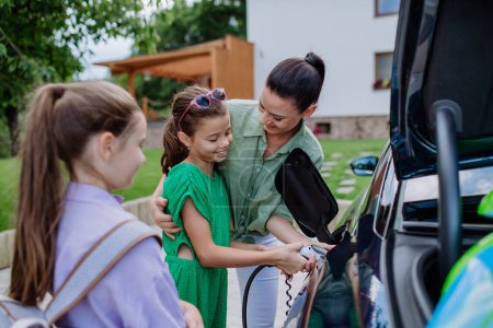 Téléchargez les photos : Mère heureuse montrant à ses filles comment recharger leur voiture électrique. - en image libre de droit