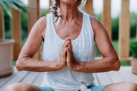Téléchargez les photos : Senior woman sitting outdoors on a terrace in summer, doing yoga exercise. - en image libre de droit