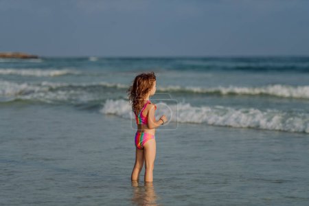 Téléchargez les photos : Petite fille en maillot de bain debout dans la mer, profiter des vacances d'été. - en image libre de droit
