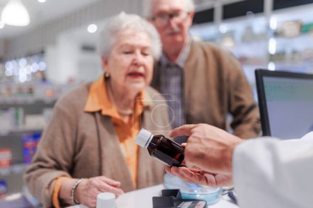 Foto de Joven farmacéutico vendiendo medicamentos a pareja mayor en una farmacia. - Imagen libre de derechos