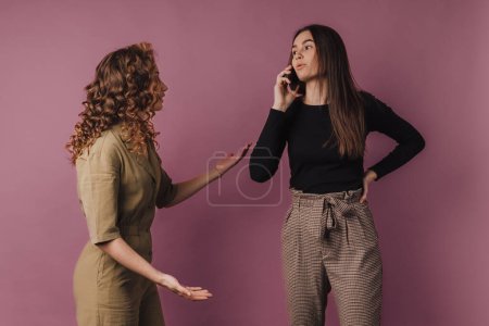 Photo for Studio shoot of two young women, one has long call with a mobile phone. - Royalty Free Image