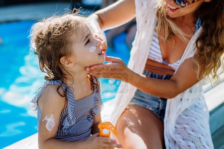 Téléchargez les photos : Une jeune mère applique une lotion solaire à sa fille. Sécurité bains de soleil dans la journée chaude. - en image libre de droit