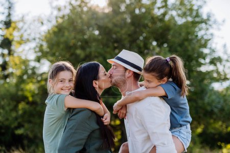 Photo for Portrait of young couple with their daughters in nature, kissing. Side view. - Royalty Free Image