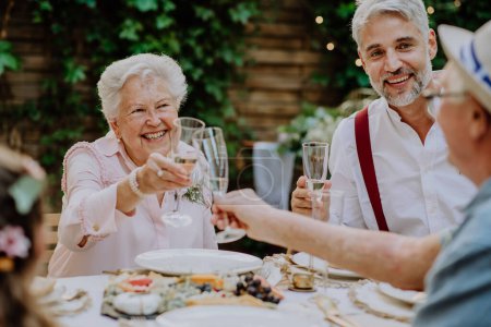 Téléchargez les photos : Mature marié toasting avec ses parents en droit à la réception de mariage à l'extérieur dans la cour. - en image libre de droit