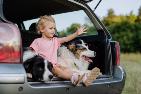 Foto de Niña y sus perros sentados en un coche, preparados para un viaje familiar, - Imagen libre de derechos