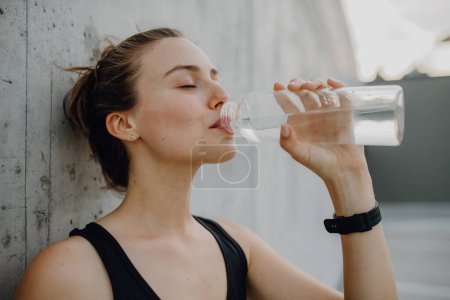 Photo for Young woman drinking water during jogging in a city, healthy lifestyle and sport concept. - Royalty Free Image