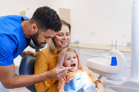 Kleines Mädchen, das mit seiner Mutter auf dem Zahnarztstuhl sitzt, während der Vorsorgeuntersuchung in der Zahnklinik.