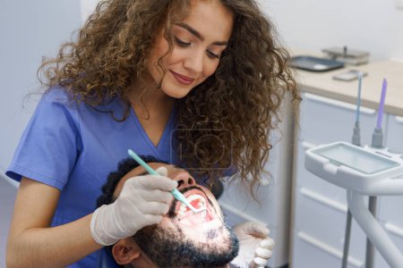 Téléchargez les photos : Jeune femme dentiste faisant un examen préventif à l'homme multiracial. - en image libre de droit