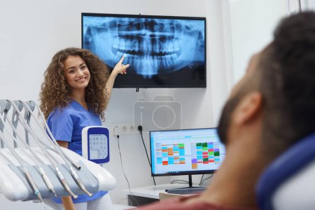 Junger Zahnarzt zeigt dem Patienten Röntgenbild.