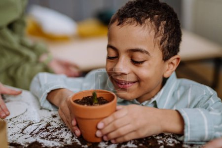 Foto de Niño feliz mirando a la planta en crecimiento en una olla de cerámica. - Imagen libre de derechos
