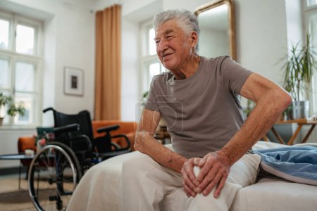 Téléchargez les photos : Portrait d'un homme âgé souffrant de douleurs au genou assis sur le lit. - en image libre de droit