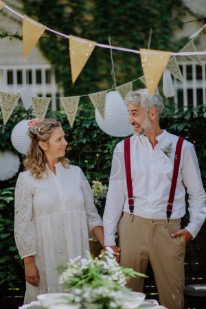 Foto de A mature bride and groom having a romantic moment at wedding reception outside in the backyard. - Imagen libre de derechos