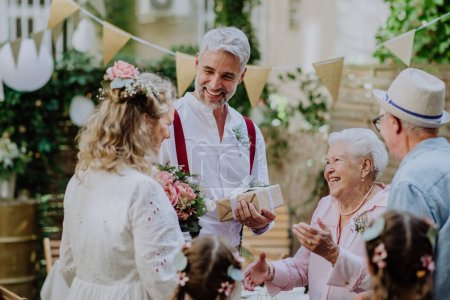 Téléchargez les photos : Une mariée mature et marié recevant des félicitations à la réception de mariage à l'extérieur dans la cour arrière. - en image libre de droit