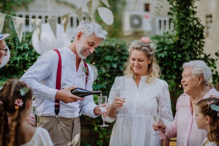 Foto de A mature bride and groom toasting with guests at wedding reception outside in the backyard. - Imagen libre de derechos