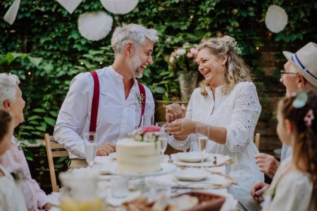 Téléchargez les photos : A mature bride and groom with guests at wedding reception outside in the backyard. - en image libre de droit
