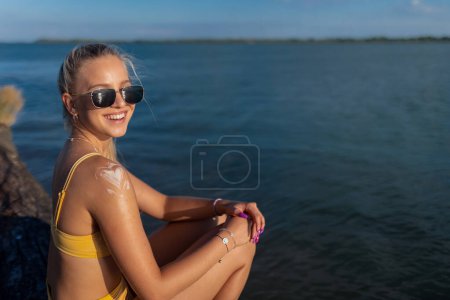 Téléchargez les photos : Close-up of young woman in yellow swimsuit applying suncreen on her skin, vacation and skin protection concept. - en image libre de droit