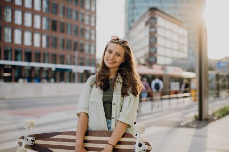 Téléchargez les photos : Jeune femme marchant en ville avec un skateboard. Culture des jeunes et concept de navettage. - en image libre de droit