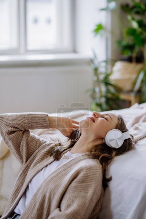 Téléchargez les photos : Jeune femme écoutant de la musique avec des écouteurs dans l'appartement. - en image libre de droit
