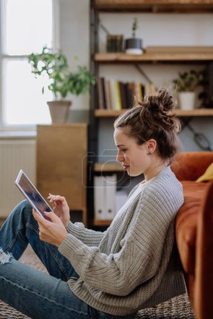 Téléchargez les photos : Jeune femme avec tablette numérique reposant dans l'appartement. - en image libre de droit