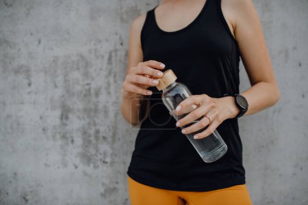 Foto de Mujer joven bebiendo agua durante el trote en una ciudad, estilo de vida saludable y concepto deportivo. - Imagen libre de derechos