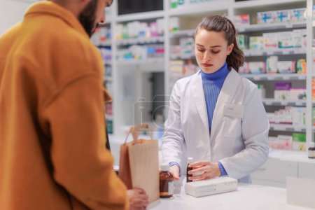 Foto de Joven farmacéutico vendiendo medicamentos a un cliente. - Imagen libre de derechos