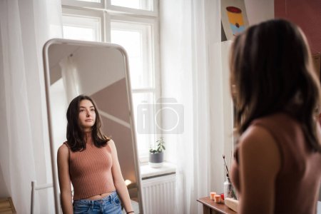 Photo for Young teenage girl looking in the mirror in the room. - Royalty Free Image