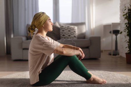 Foto de Mujer joven con cáncer sentada después de hacer yoga en el apartamento. - Imagen libre de derechos