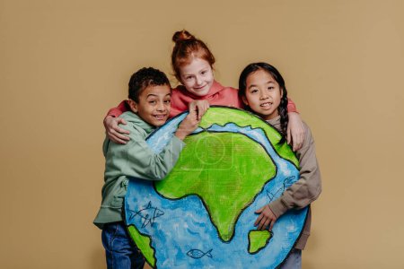 Foto de Retrato de tres niños con modelo de Tierra, sesión de estudio. Concepto de diversidad en una amistad. - Imagen libre de derechos