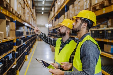 Téléchargez les photos : Warehouse workers checking stuff in warehouse with digital system in a tablet. - en image libre de droit