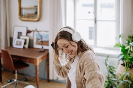 Foto de Mujer joven escuchando música a través de auriculares en el apartamento. - Imagen libre de derechos