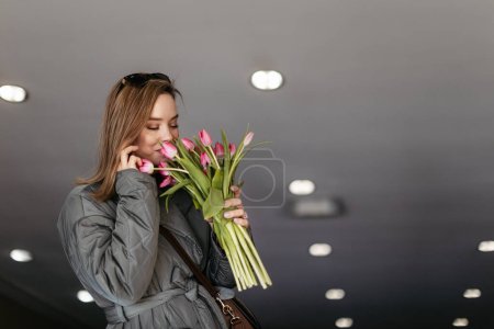 Foto de Mujer joven llamando en una ciudad con ramo de tulipanes. - Imagen libre de derechos