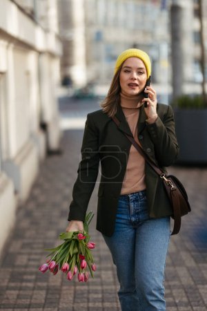 Téléchargez les photos : Jeune femme marchant dans une ville avec des tulipes et appelant. - en image libre de droit