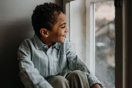 Photo for Little multiracial boy looking out of the window. - Royalty Free Image